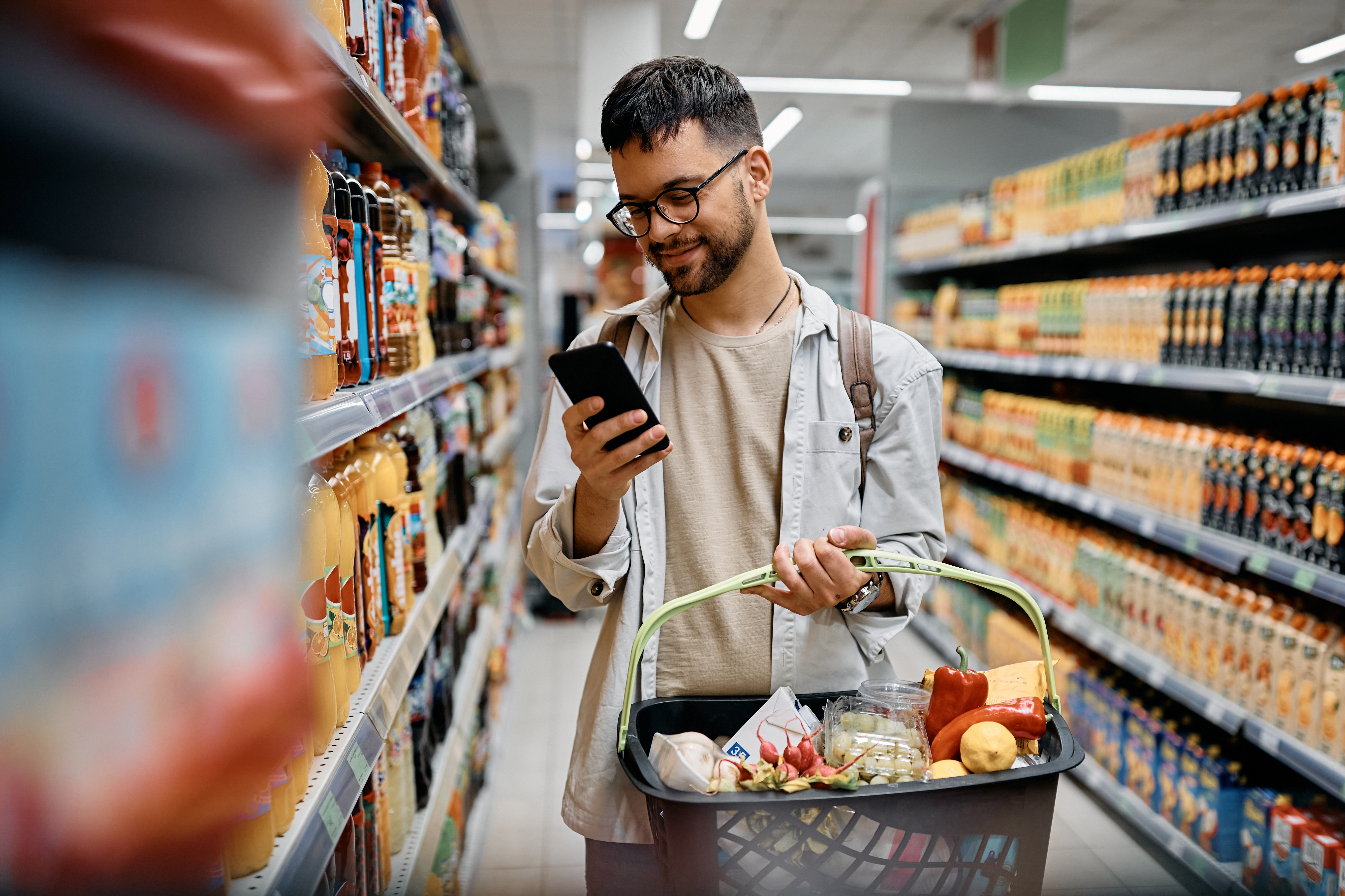 Um homem jovem mexendo no celular enquanto realiza compras no mercado