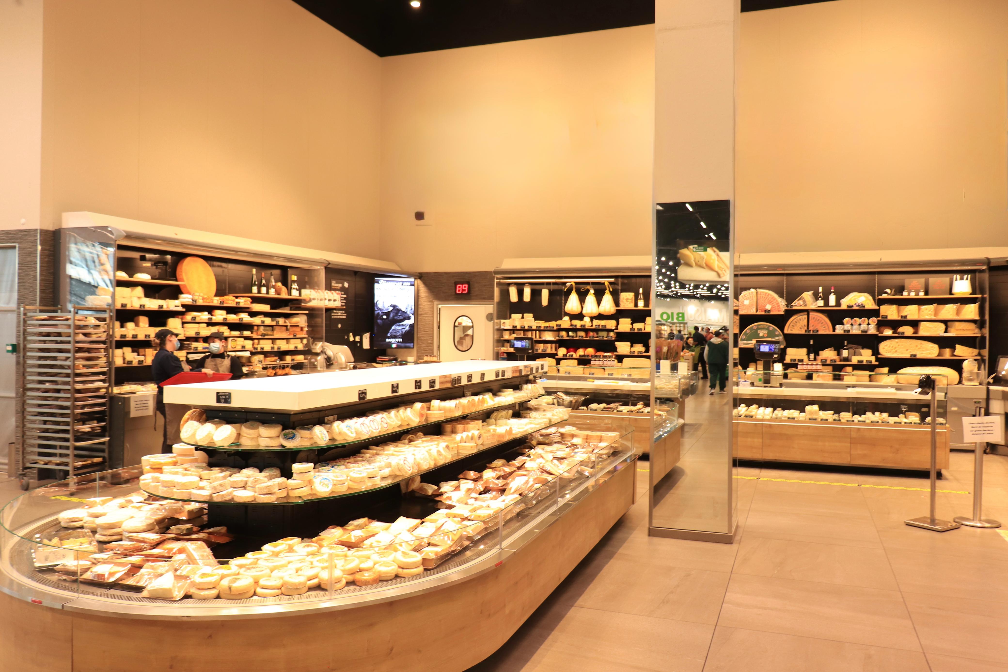 Interior de uma loja de supermercado que mostra uma grande variedade de quejos, com gôndolas verticais e horizontais