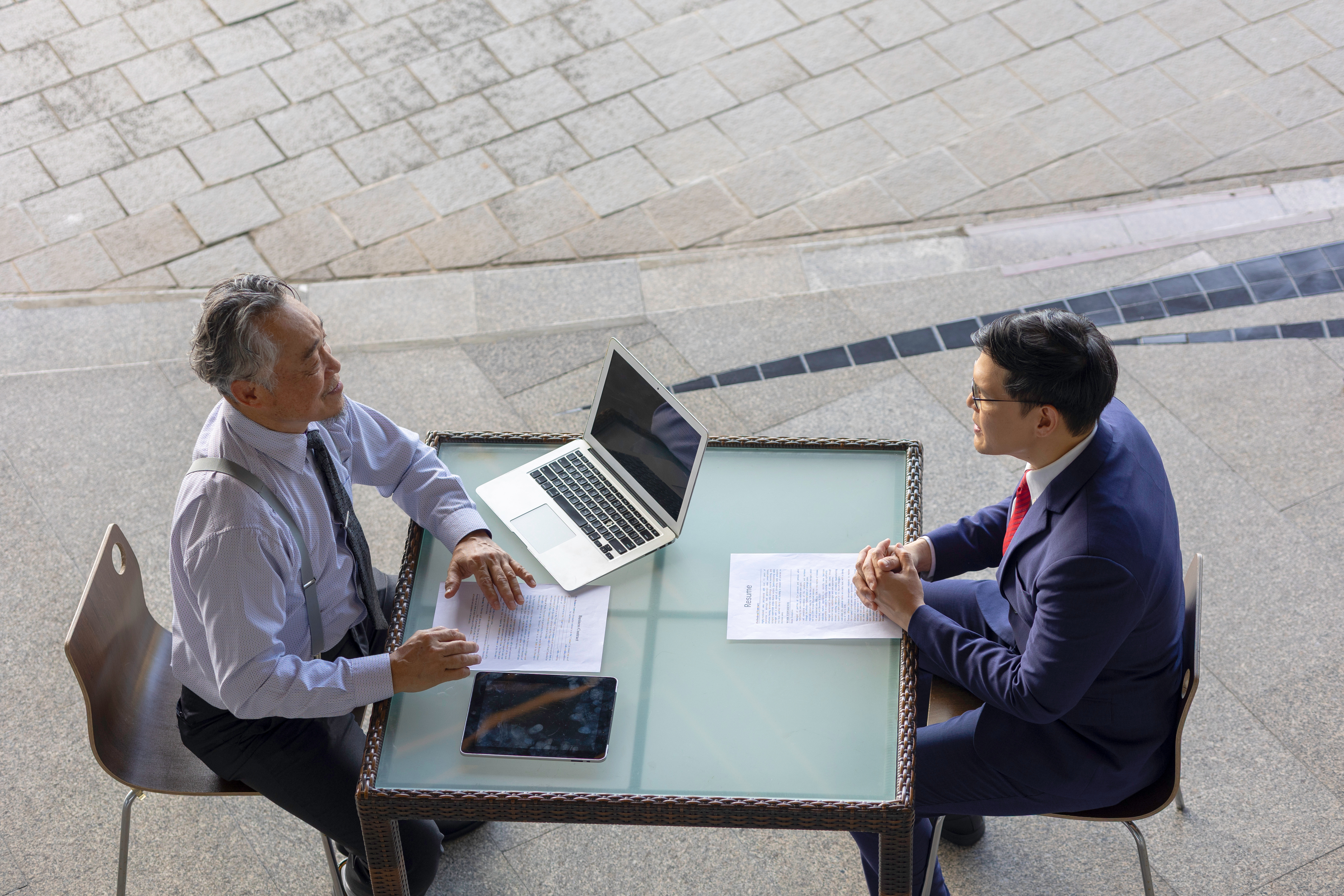 Dois homens sentados à mesa com vestimentas formais e um computador conversando